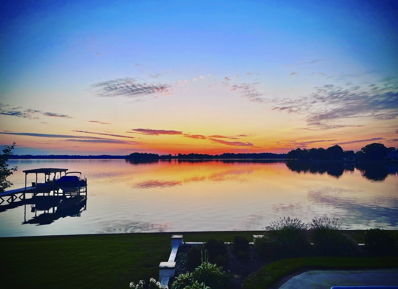 Sunrise over Lake Norman, a boat dock reflected in still water under a blue sky turning gold at the horizon