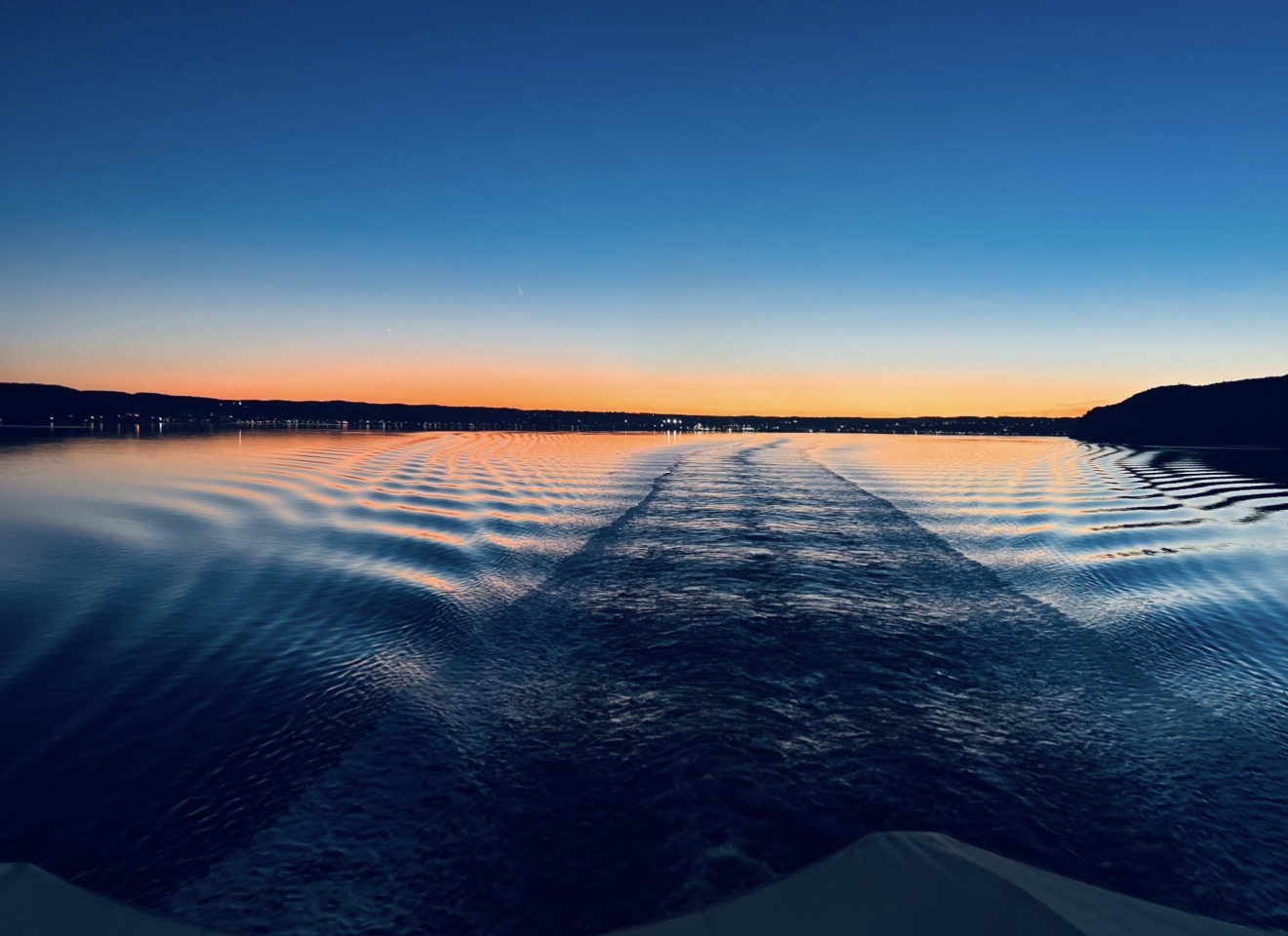 A boat's wake stretching across the lake toward an orange horizon at dawn